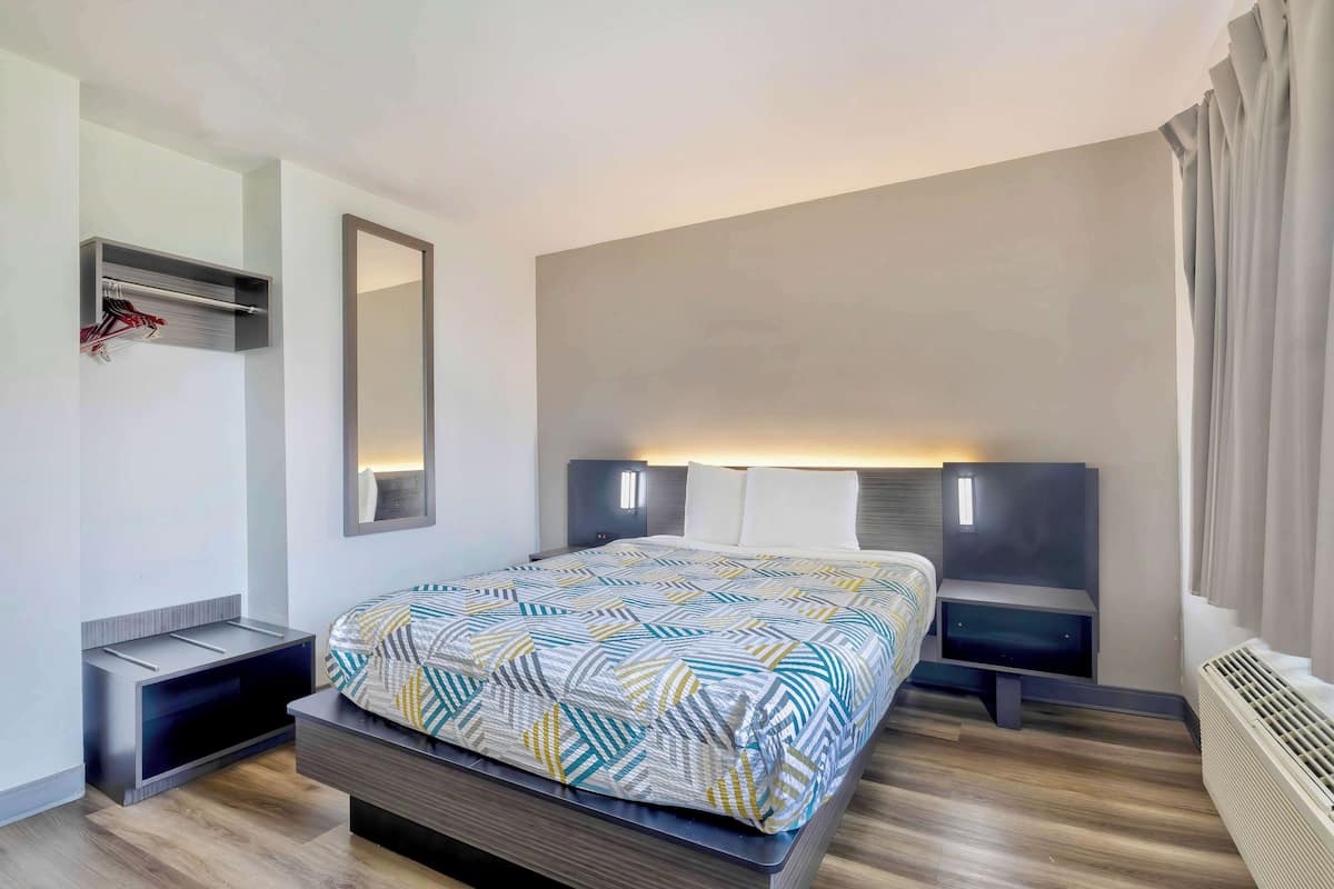 Una habitación de hotel moderna con cama, mesitas de noche, un espejo y un calentador integrado.