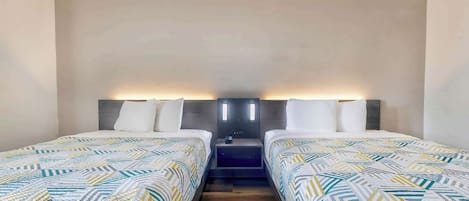 Habitación de hotel con dos camas, una mesita de noche y una lámpara fijada a la pared.