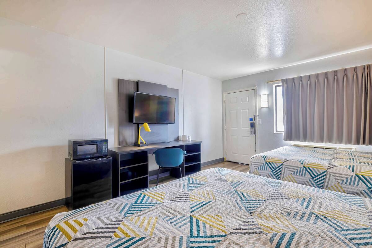 A hotel room with two beds, a desk, a TV, and a window with curtains.