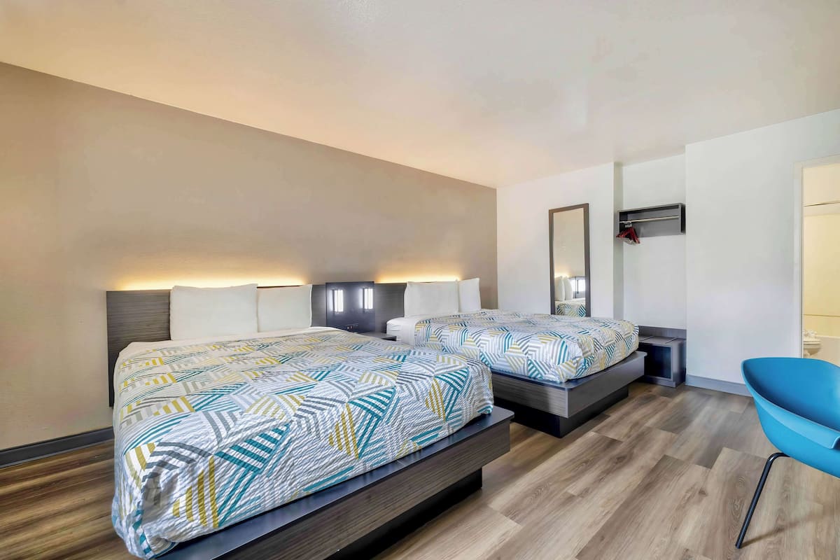 Una habitación de hotel con dos camas, una silla azul, un espejo y un calentador fijado a la pared.