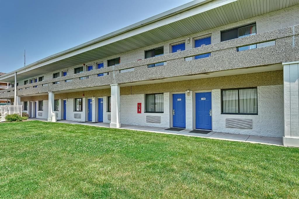 A row of motel rooms with individual doors, a flat roof, and a grassy area in front.