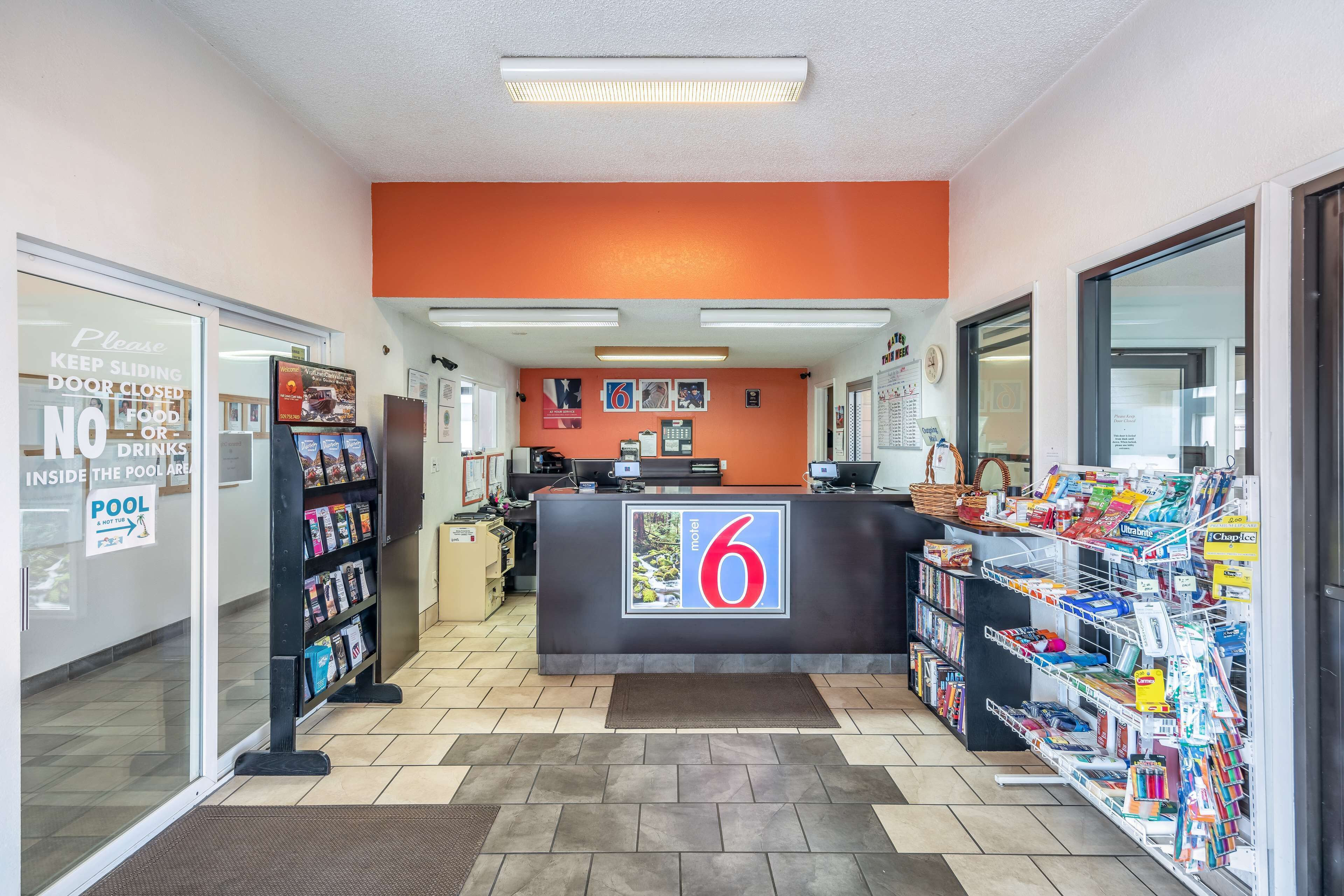 A motel lobby with a reception desk, a pool sign, and a variety of amenities including a vending machine and a magazine rack.