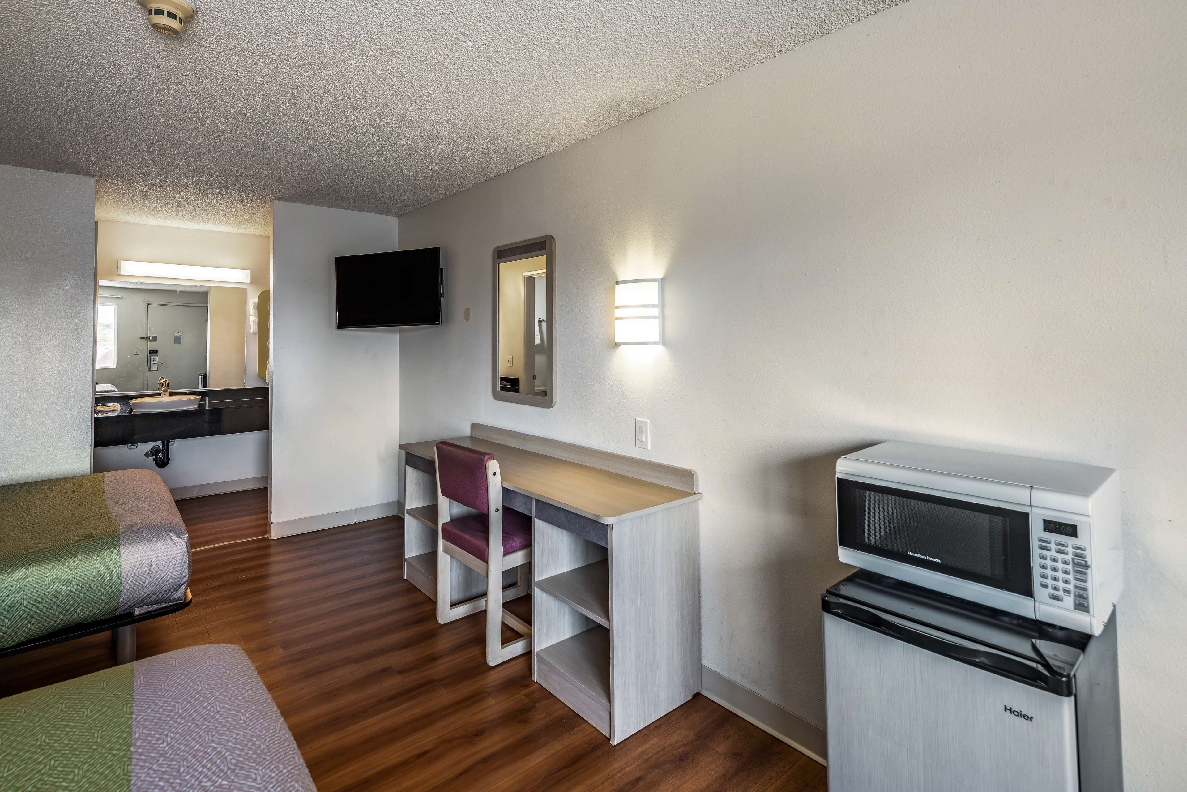 Une chambre d’hôtel compacte comprenant un lit, un bureau avec une chaise, un four à micro-ondes et un petit réfrigérateur.