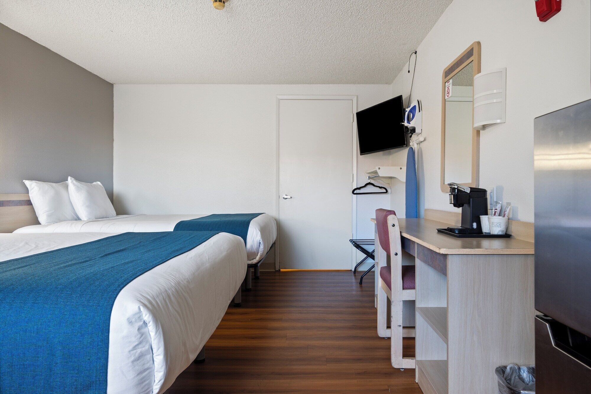 Habitación de hotel con cama, escritorio con cafetera, televisor y espejo.
