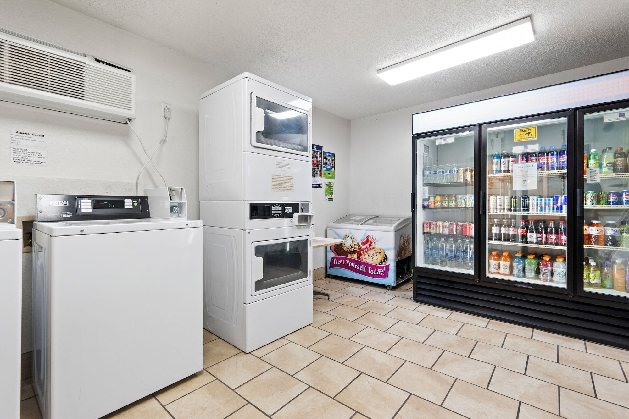Un cuarto de lavado con lavadoras y secadoras apiladas, un microondas y un refrigerador lleno de bebidas.