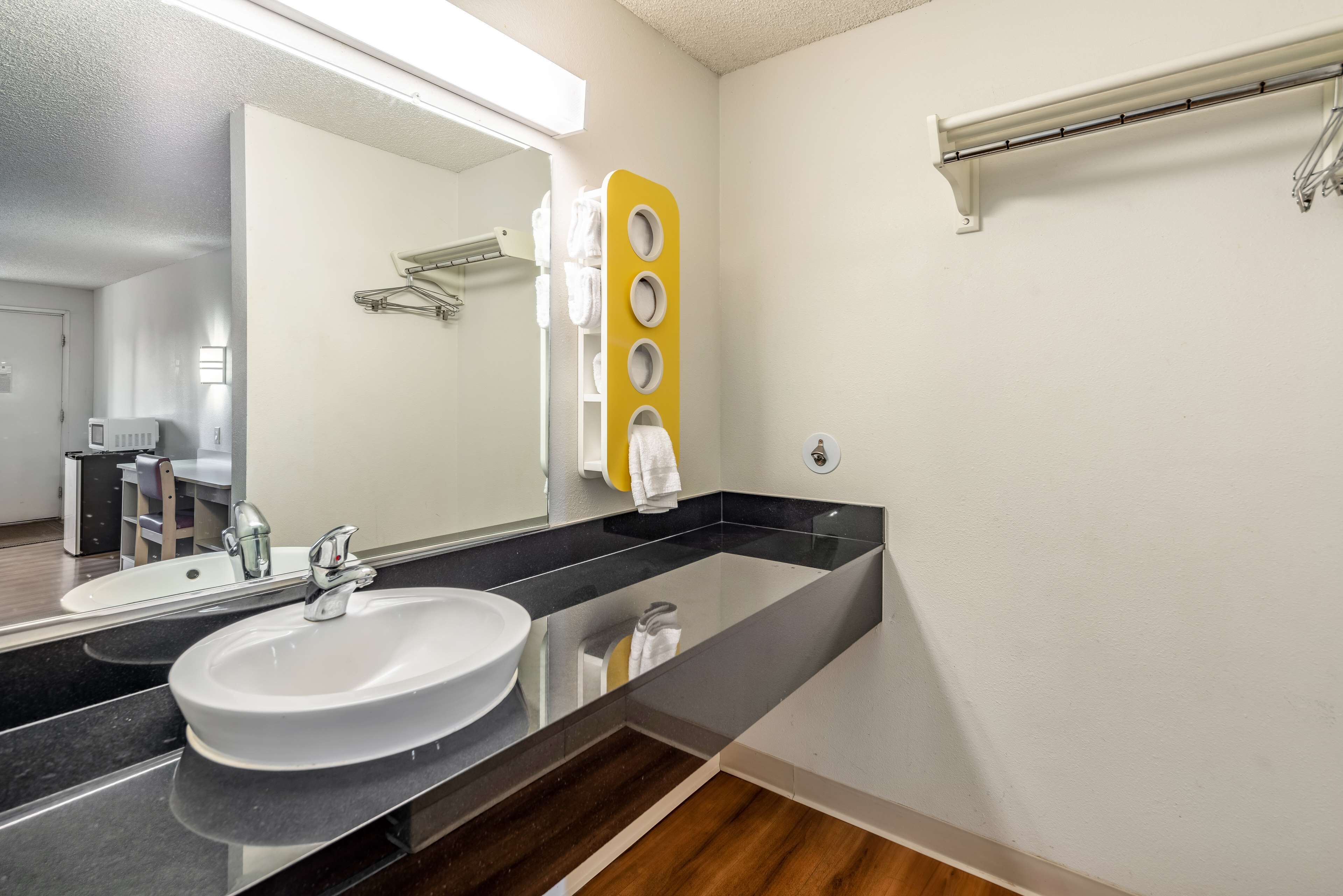A modern bathroom with a large mirror, two sinks, a towel rack, and a towel dispenser.