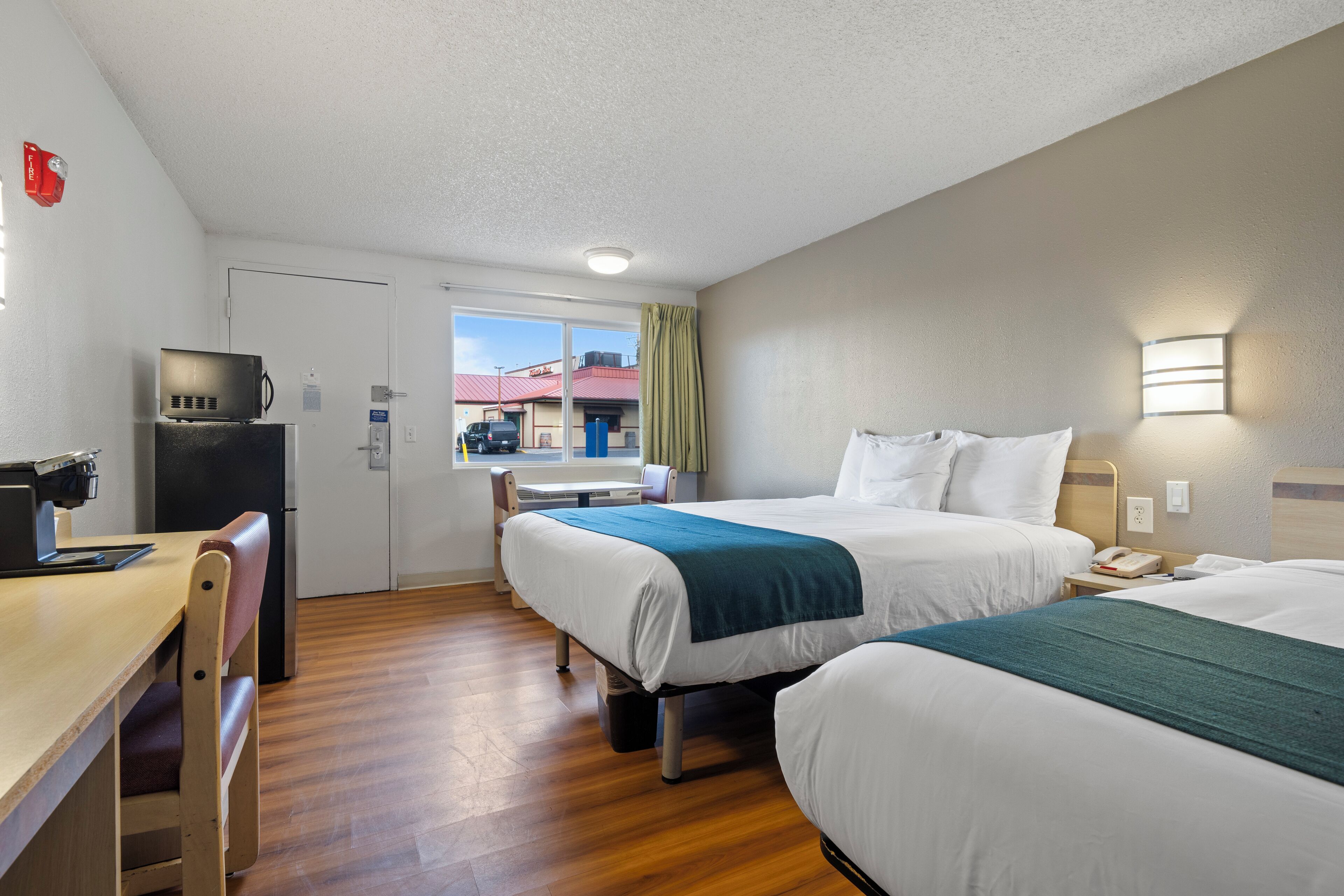 A hotel room with two beds, a desk, a microwave, and a window with a view of a building.
