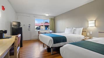 A hotel room with two beds, a desk, a microwave, and a window with a view of a building.