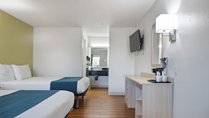 Une chambre d’hôtel avec deux lits, un bureau, un miroir et une télévision.