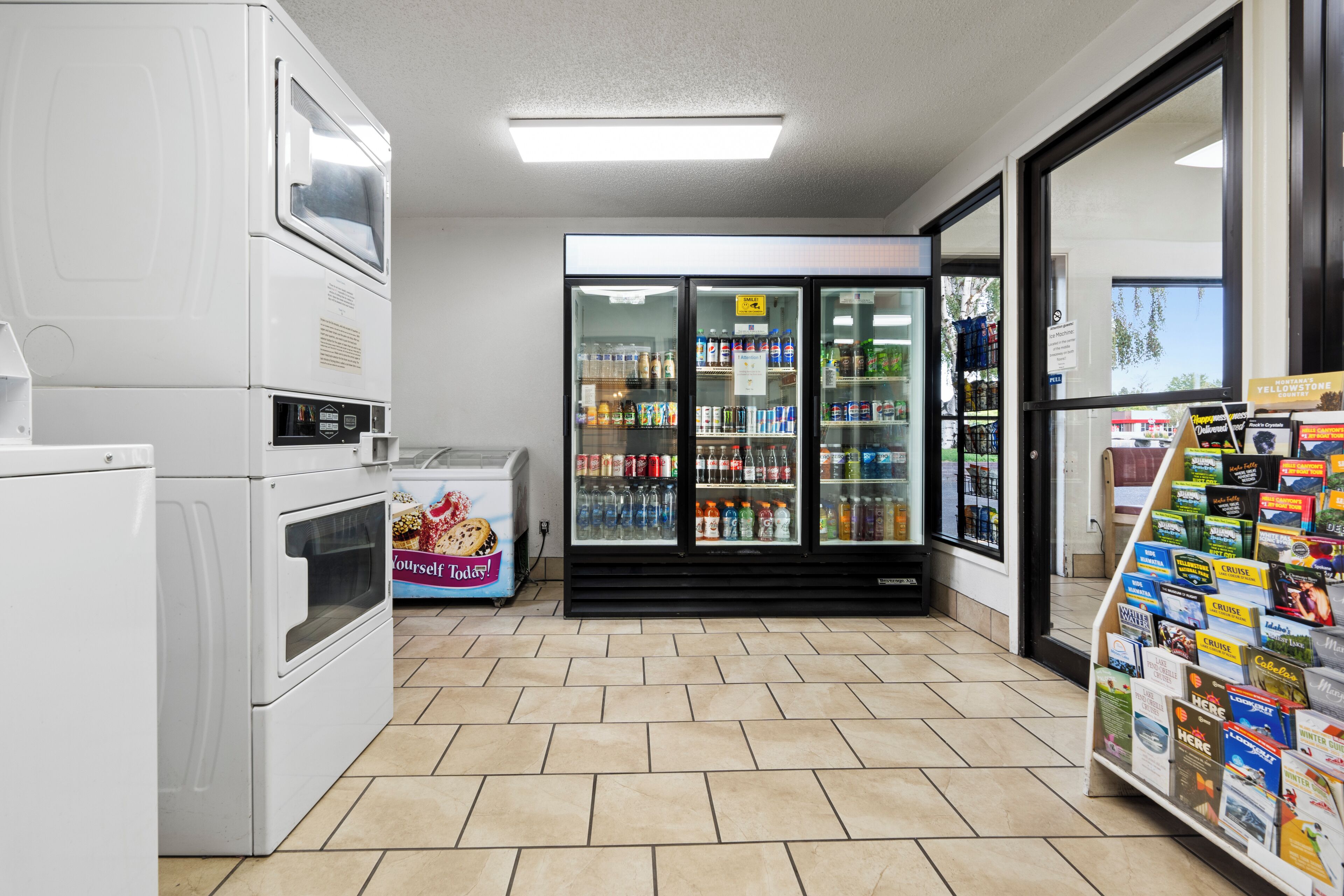 A laundromat with a self-service dryer, a refrigerated beverage cooler, and a display of travel brochures.