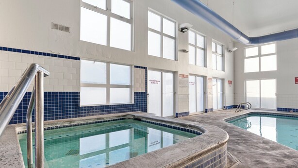 Une piscine intérieure avec des parois en verre transparent, un sol carrelé et une rambarde métallique.
