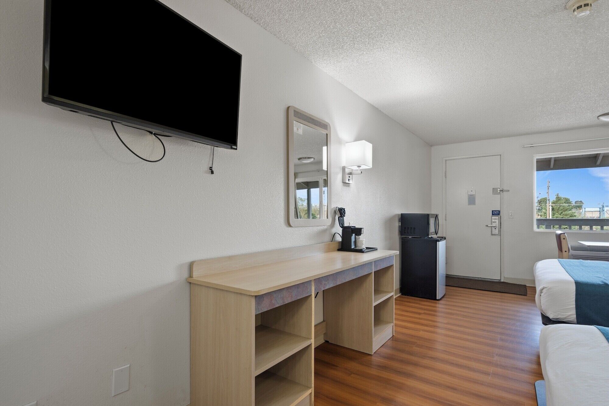 A hotel room with a flat-screen TV, a mirror, a coffee maker, a desk, and a bed.