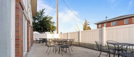 An outdoor patio with metal tables and chairs, a brick building, and a white fence.