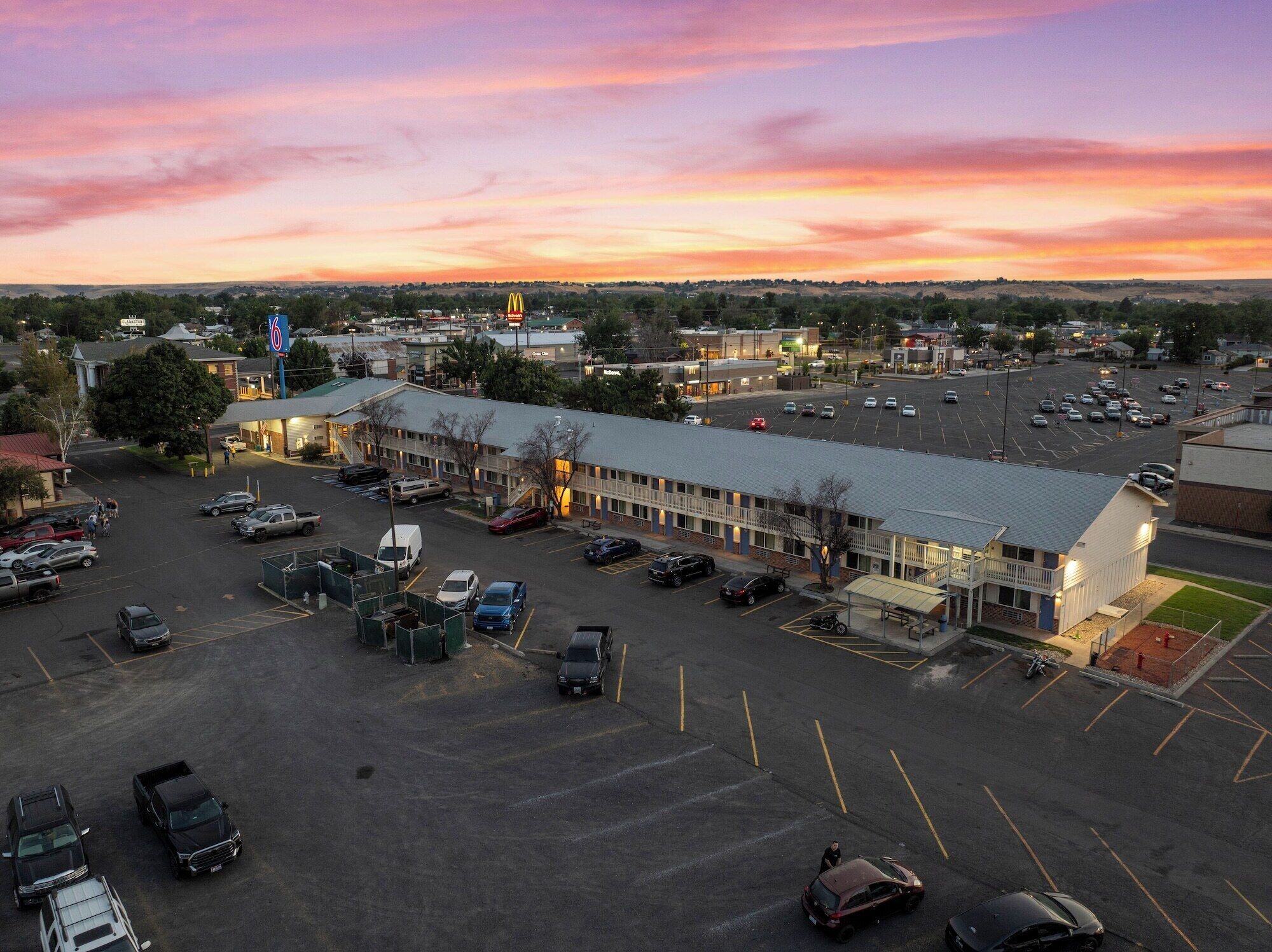 A large parking lot with multiple cars and a building with a flat roof and a sign with a number.