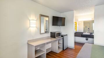 A compact hotel room with a kitchenette, a flat-screen TV, a mirror, and a bed.