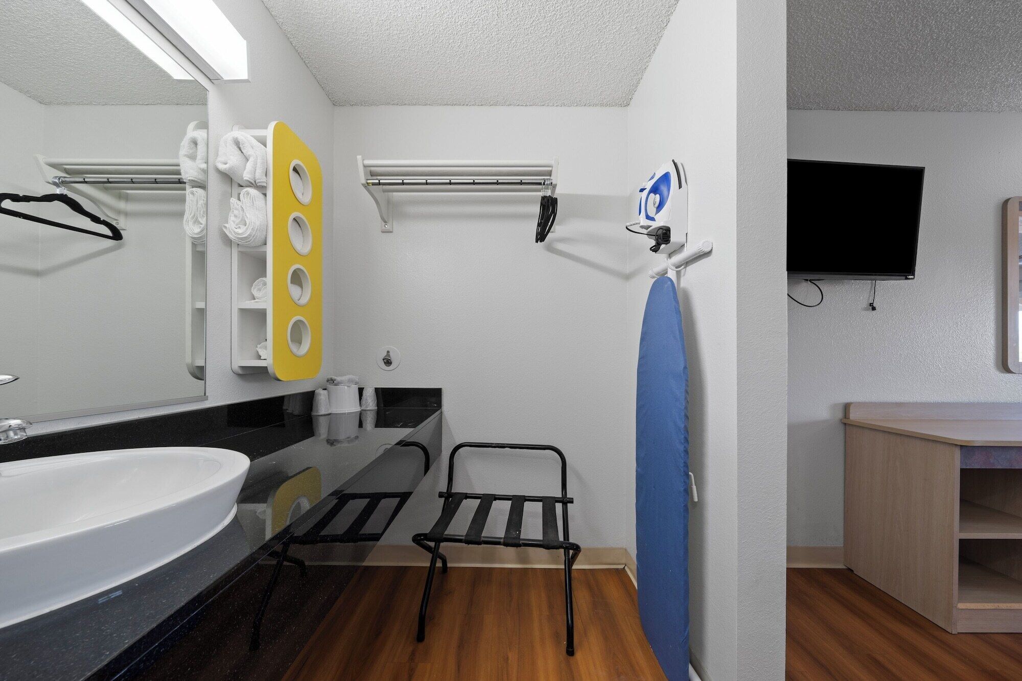 A modern bathroom with a large mirror, a sink, a towel rack, a drying rack, a shower area, and a television mounted on the wall.