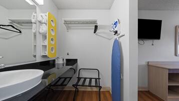 A modern bathroom with a large mirror, a sink, a towel rack, a drying rack, a shower area, and a television mounted on the wall.