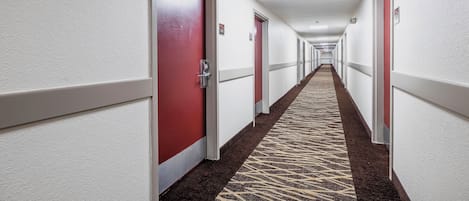 Un couloir d’hôtel avec des portes, un sol recouvert de moquette et un plafond doté d’un éclairage encastré.