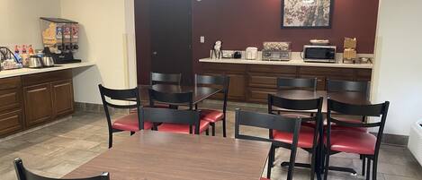 A dining area with a table and chairs, a kitchen area with appliances, and a door leading to another room.