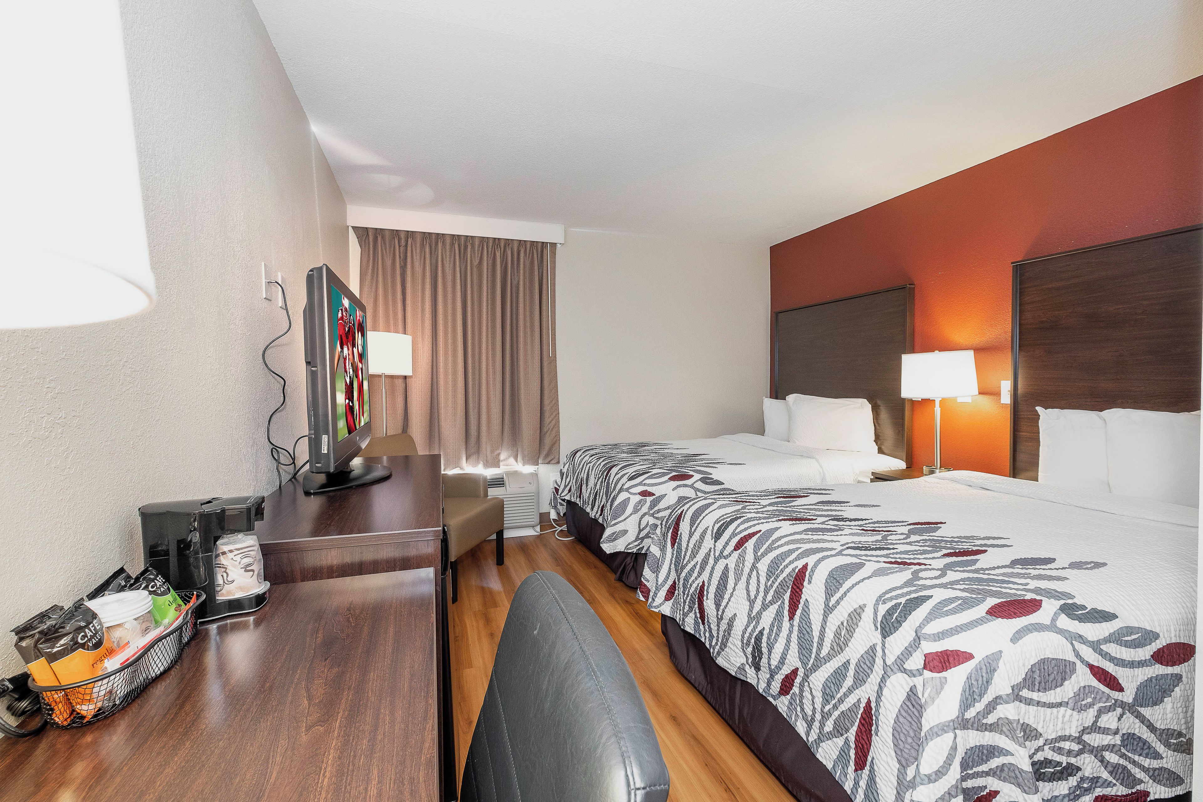 A hotel room with a bed, bedside table, lamp, and a desk with a coffee machine.
