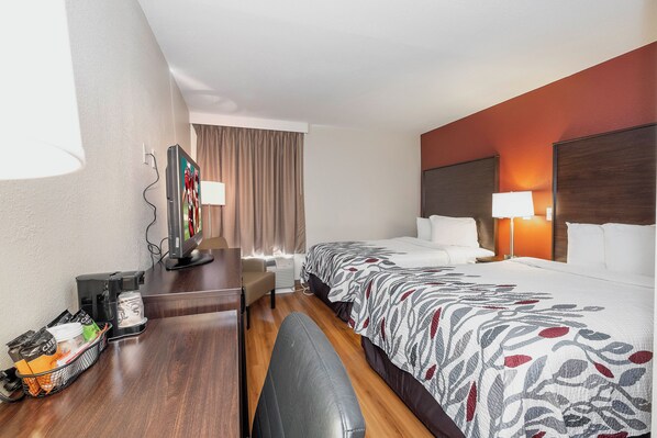 A hotel room with a bed, bedside table, lamp, and a desk with a coffee machine. - Red Roof Inn Roanoke Rapids (Roanoke Rapids)