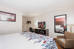 Una habitación de hotel con cama, televisión, escritorio con silla y espejo.