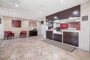 A reception area with a check-in desk, two red chairs, a stone wall, and a Red Roof Inn sign. - Red Roof Inn Roanoke Rapids (Roanoke Rapids)