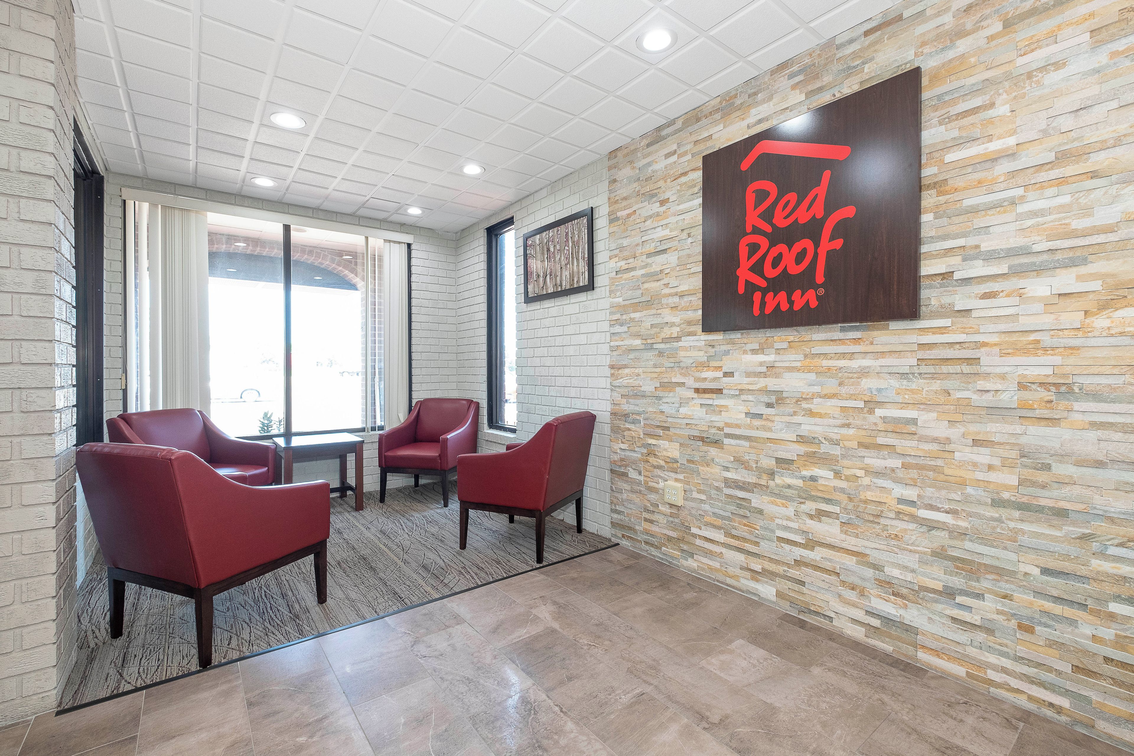 A Red Roof Inn lobby with a stone wall, three red chairs, and a large sign.