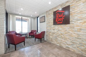 A Red Roof Inn lobby with a stone wall, three red chairs, and a large sign. - Red Roof Inn Roanoke Rapids (Roanoke Rapids)