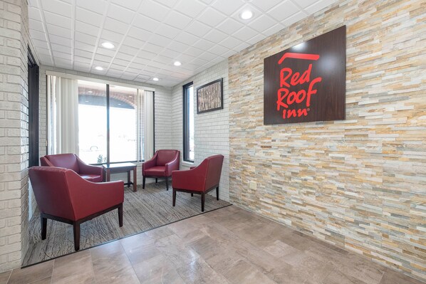 A Red Roof Inn lobby with a stone wall, three red chairs, and a large sign. - Red Roof Inn Roanoke Rapids (Roanoke Rapids)