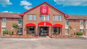 Ett Red Roof Inn-hotell med en fasad av tegel, röda markiser och en klarblå himmel.