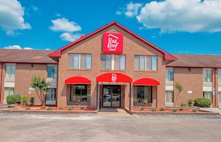 Un hotel Red Roof Inn con fachada de ladrillo, toldos rojos y un cielo azul despejado.