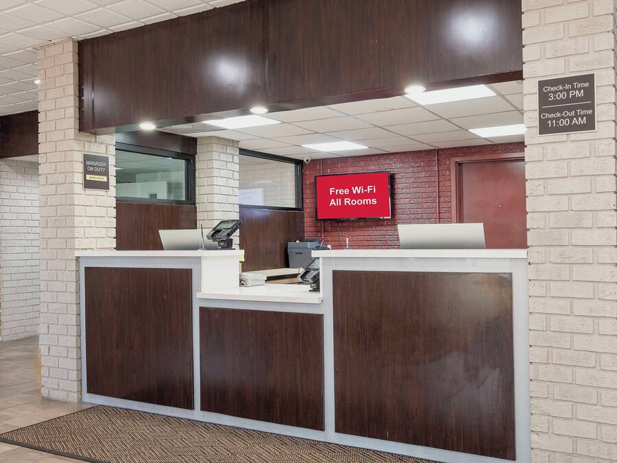 Una recepción con una pantalla digital que muestra 'Wi-Fi gratis en todas las habitaciones' y un cartel con los horarios de registro de entrada y salida.