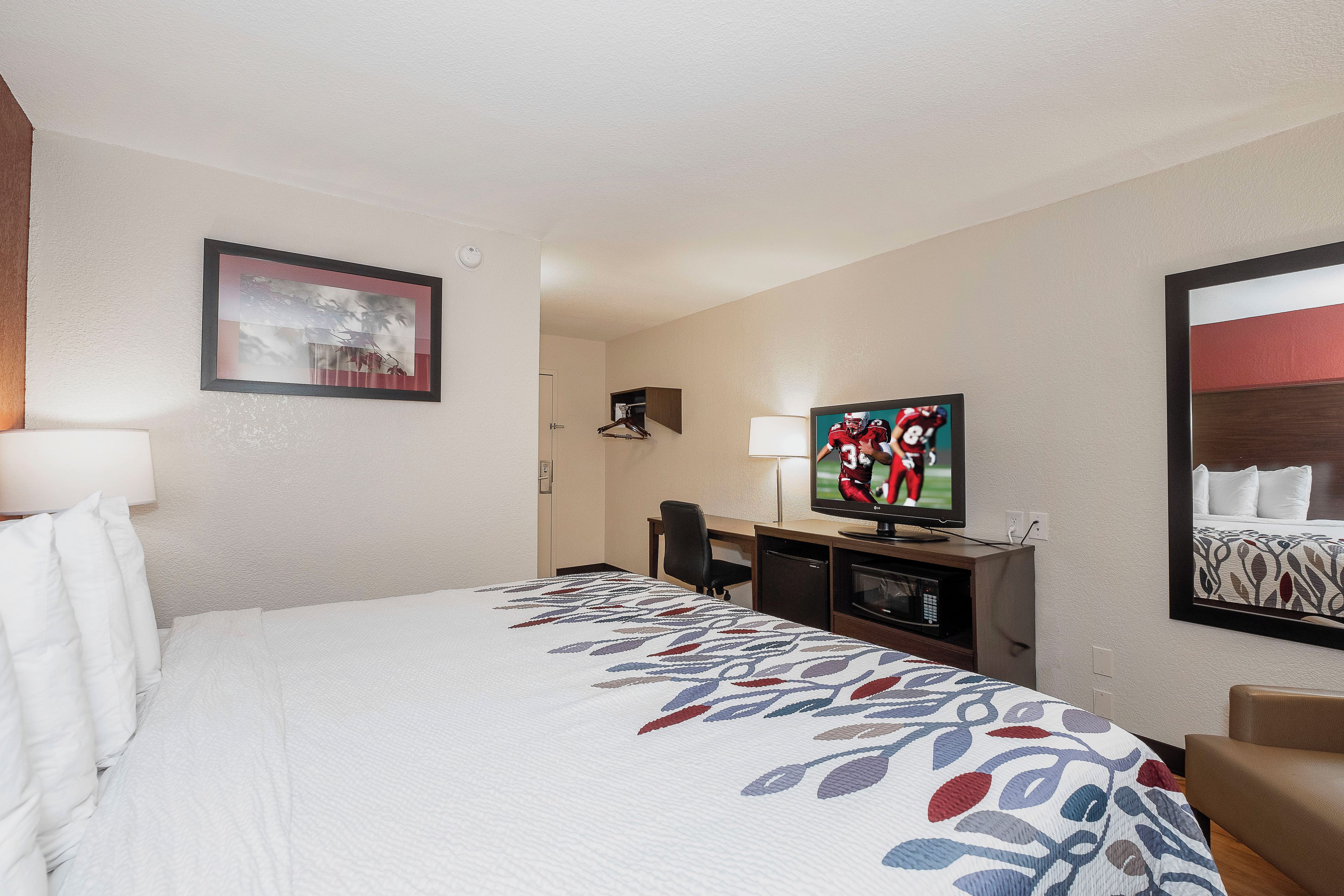 Una habitación de hotel con una cama, un escritorio, un televisor y un cuadro en la pared.