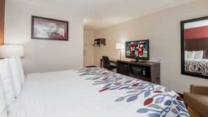 Ett hotellrum med en säng, ett skrivbord, en tv och en inramad tavla på väggen.