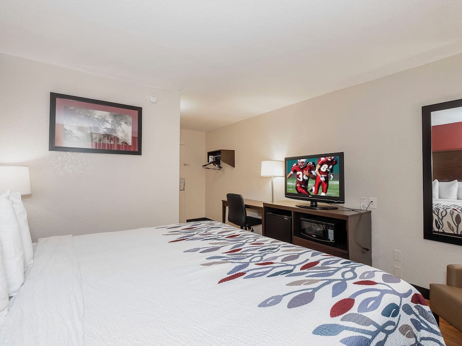 A hotel room with a bed, a desk, a television, and a framed picture on the wall.