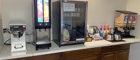 A self-service beverage station with a coffee machine, a refrigerator, and a snack dispenser.