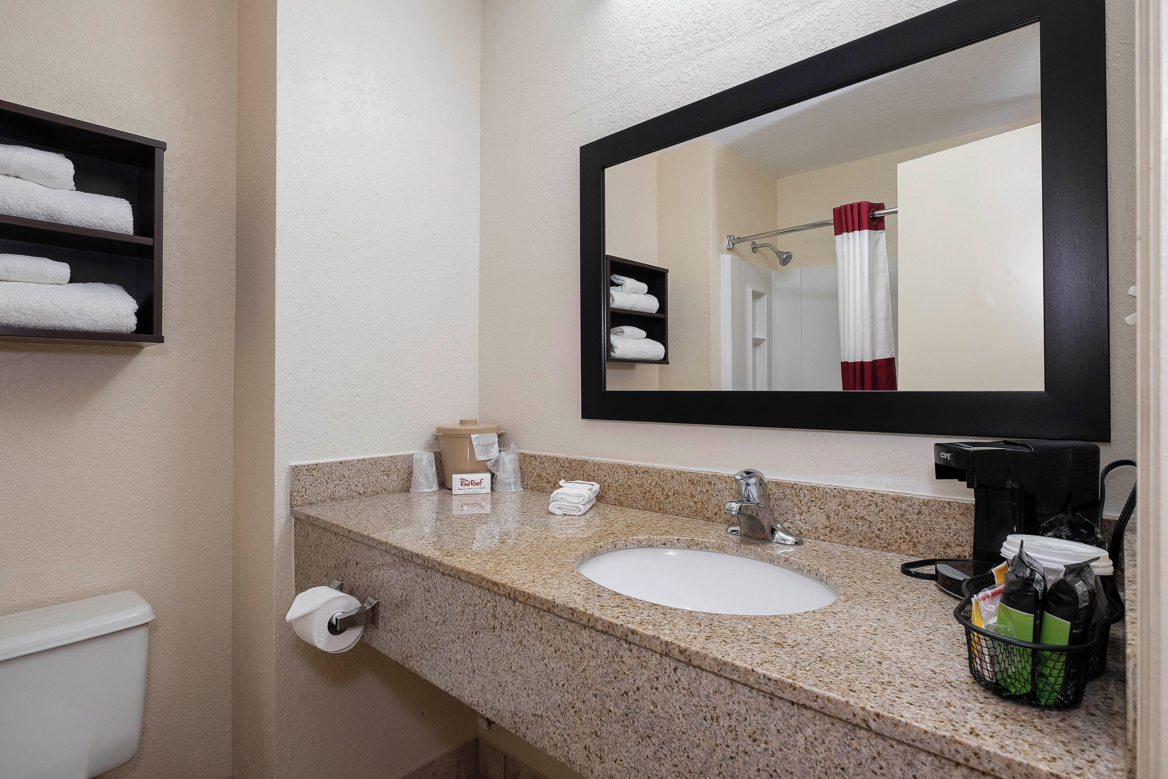 Ein Hotelbad mit einer Granit-Arbeitsplatte, einem Waschbecken, einem Spiegel, einem Handtuchhalter und einem Toilettenpapierhalter.