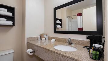 Ein Hotelbad mit einer Granit-Arbeitsplatte, einem Waschbecken, einem Spiegel, einem Handtuchhalter und einem Toilettenpapierhalter.
