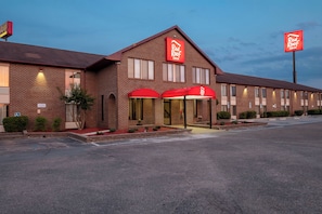 Un Red Roof Inn con fachada de ladrillo, múltiples ventanas y un estacionamiento al frente.