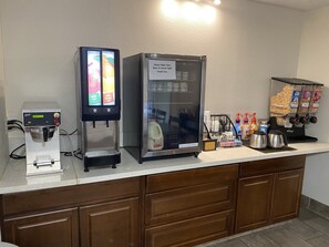 Una estación autoservicio con una máquina de café, un dispensador refrigerado de bebidas y un dispensador de aperitivos.