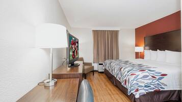 Una habitación de hotel con cama, escritorio, televisor, lámpara y ventana con cortinas.