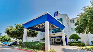 A modern hotel entrance with a blue canopy, a number '6' sign, and a 'Welcome' sign.