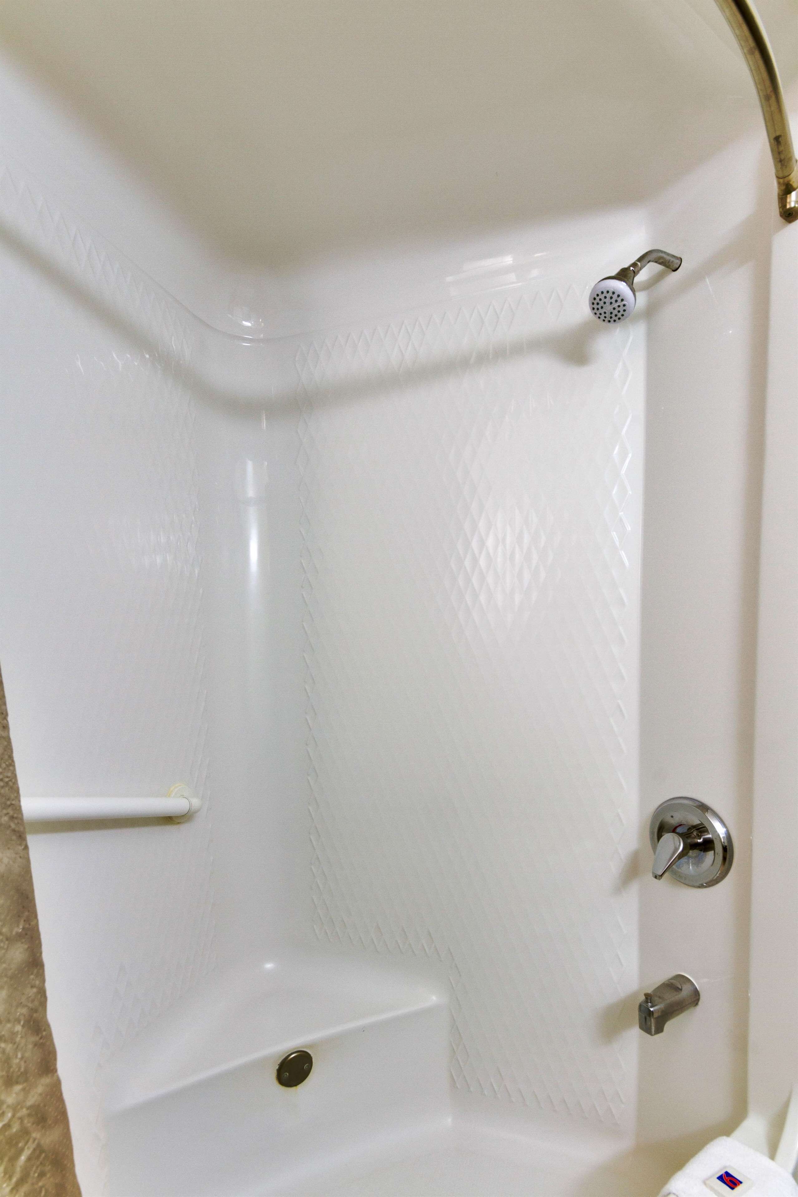 A corner of a white bathtub with a showerhead, a faucet, and a shelf.