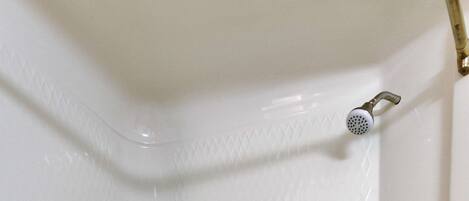 A corner of a white bathtub with a showerhead, a faucet, and a shelf.
