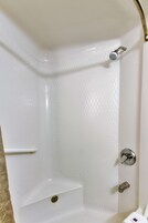 A corner of a white bathtub with a showerhead, a faucet, and a shelf.