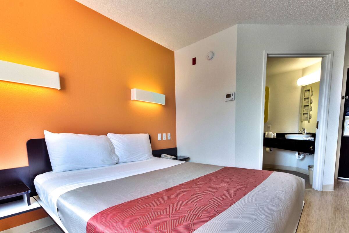 Una camera d'albergo con un letto, un comodino e un bagno visibile attraverso una porta aperta.