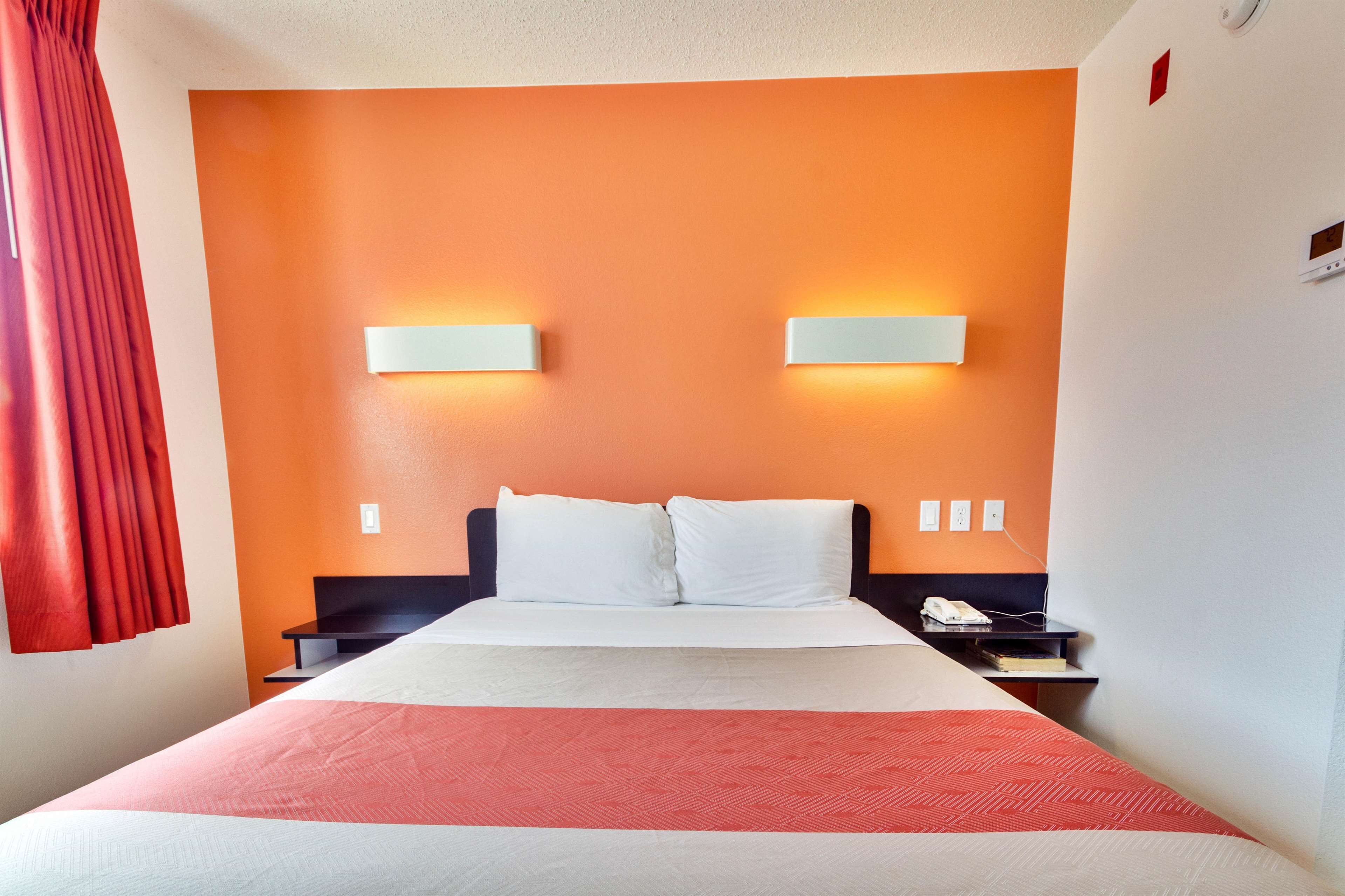 A hotel room with a bed, two bedside tables, a nightstand, a red curtain, and wall-mounted lights.