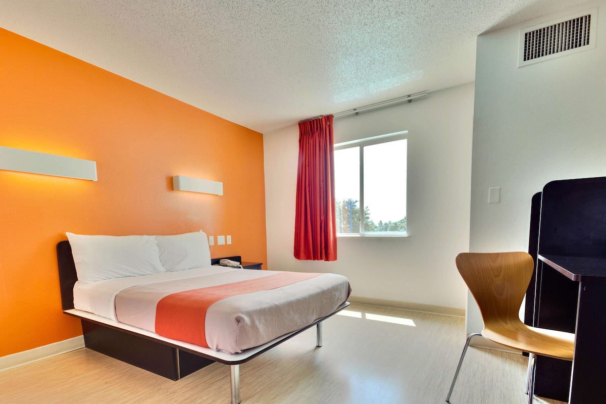Una camera d'albergo moderna con un letto, una sedia e una finestra con tende.