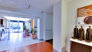 A hotel lobby with a coffee station, a reception desk, and a view of the outside.